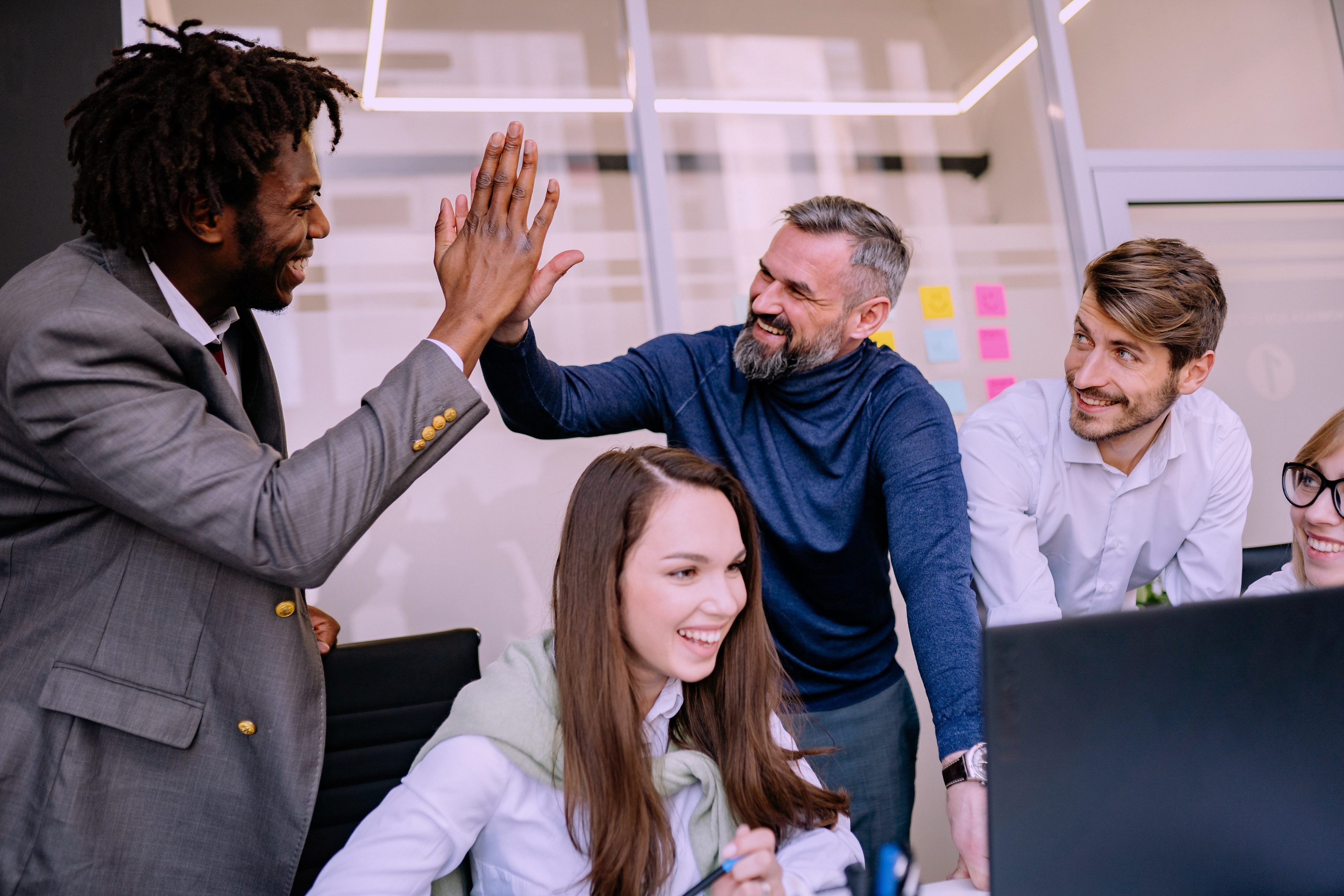 Colleagues around a desk in an office, two of them high-fiving over a laptop